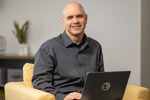 Color photo of Robert Hart, sitting on a yellow couch with a laptop.