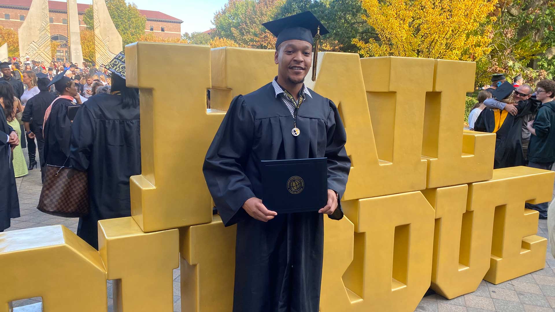 TJ Gilmore stands in front of a Hail Purdue sign after receiving his diploma at graduation.