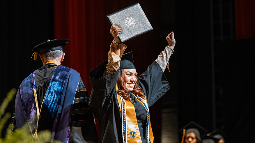 A Purdue Global graduate holds her diploma in the air and smiles