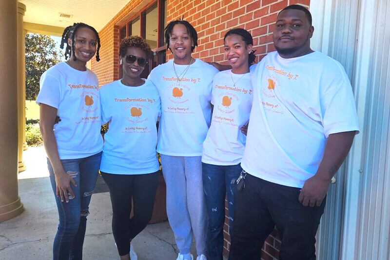 Theo Gilmore Jr. (center) stands with four other wearing matching t-shirts outside a brick building