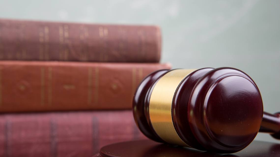 A gavel sits on a desk in front of some law books.