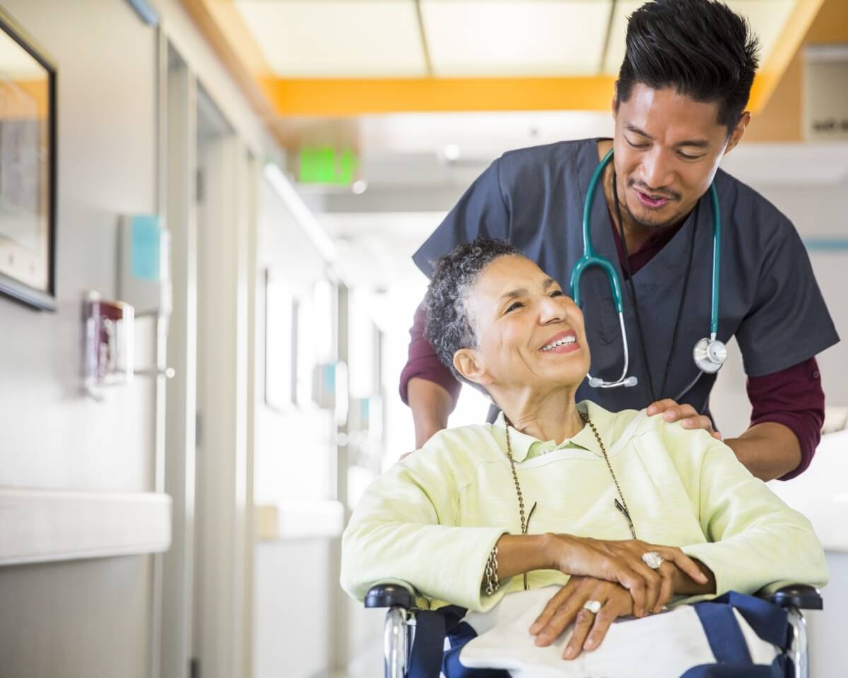 A nurse talks to a patient in a wheelchair in a medical facility