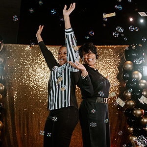 two smiling Purdue Global graduates dancing at the Black and Gold celebration, surrounded by black and gold ballooons