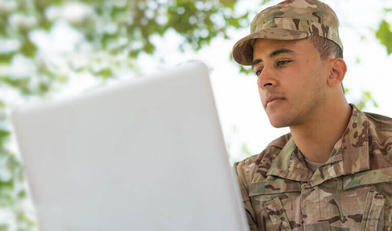 military student in uniform working on a laptop outside