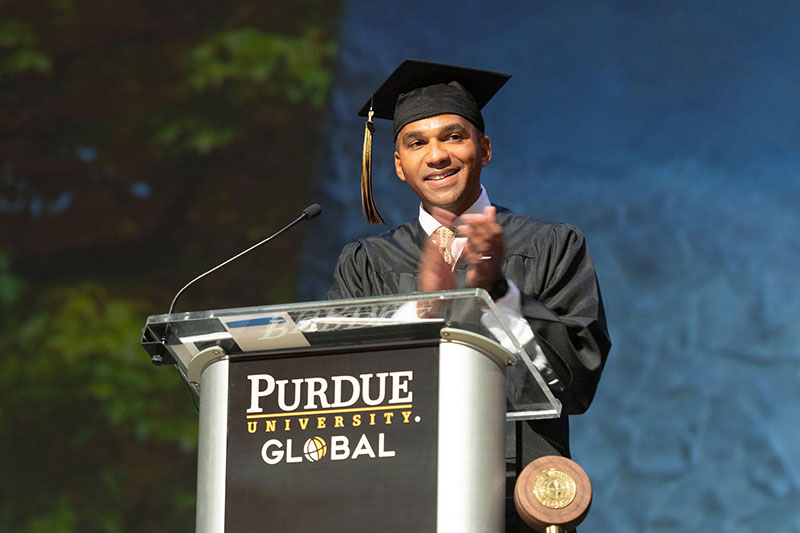 Klevin Gumbs standing at a podium speaking at graduation