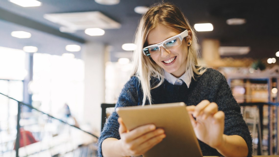 A woman wearing smart glasses while working on a tablet.