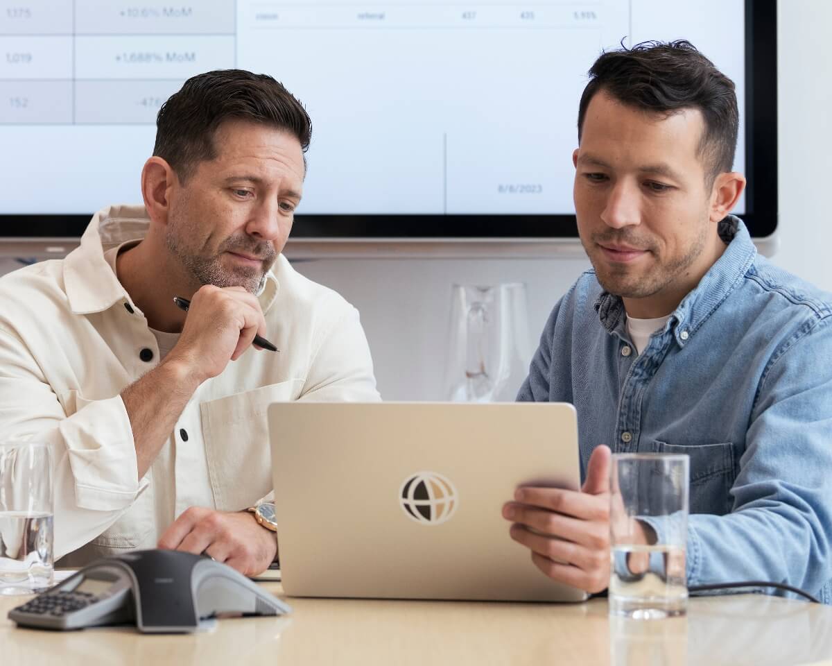 Two professionals looking at a laptop in front of a smartboard in an office