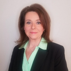 Woman in a green shirt with a black jacket on a gray background.