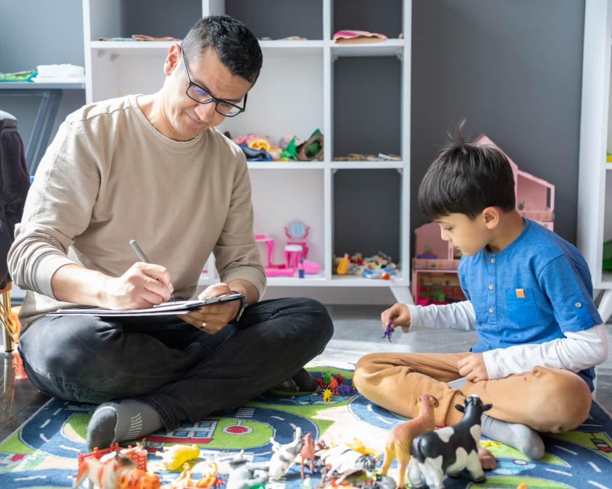 A professional takes notes while observing a child playing with toys