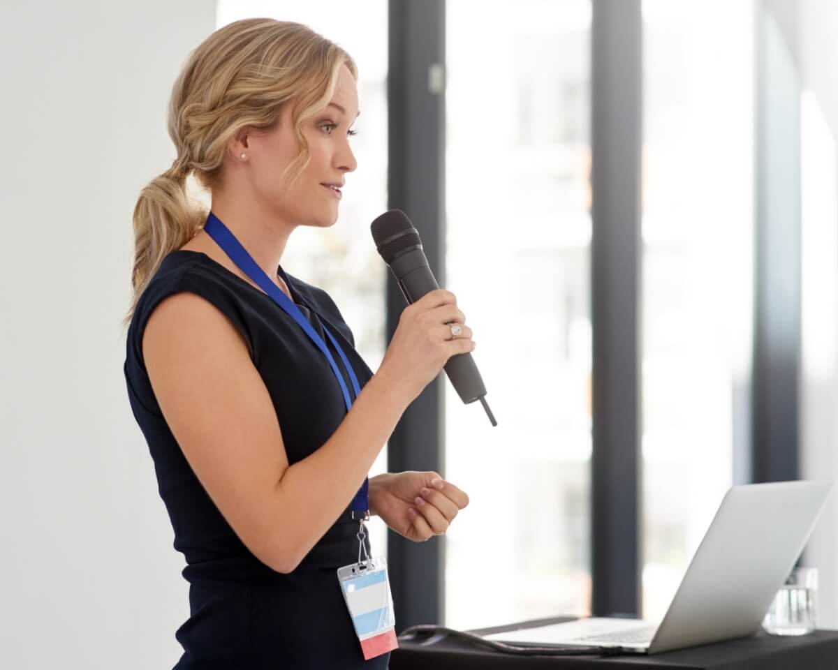 A professional with an open laptop gives a speech while holding a microphone