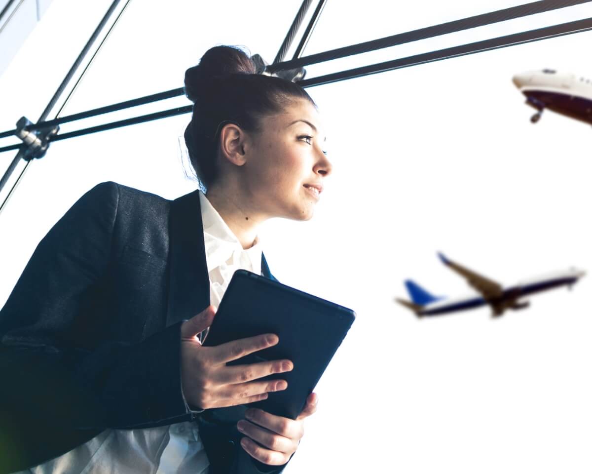 Prefessiona holding a tablet looks at airplanes in flight beyond a large window