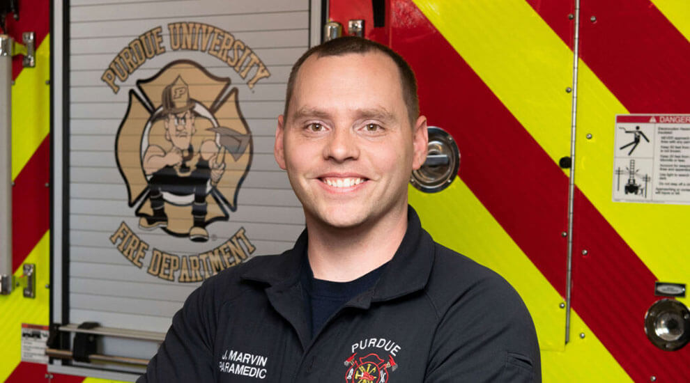 Purdue Global graduate Justin Marvin in front of Purdue fire truck