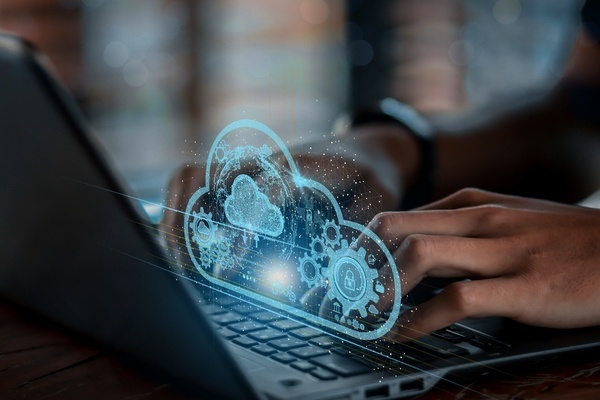 Person typing with a holographic image of a cloud surrounded by digital icons.