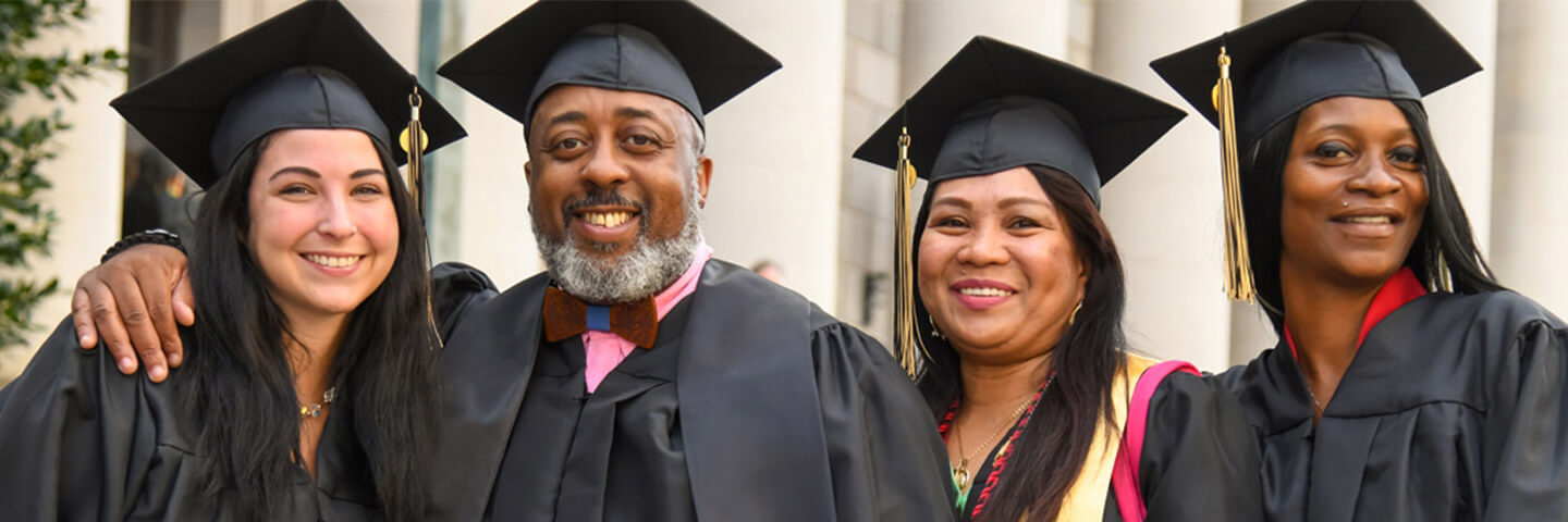 Four Purdue Global graduates in their graduation robes outside a commencement ceremony.