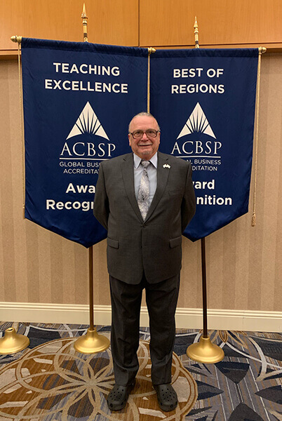 Stanley Self stands in front of ACBSP award banners at a conference