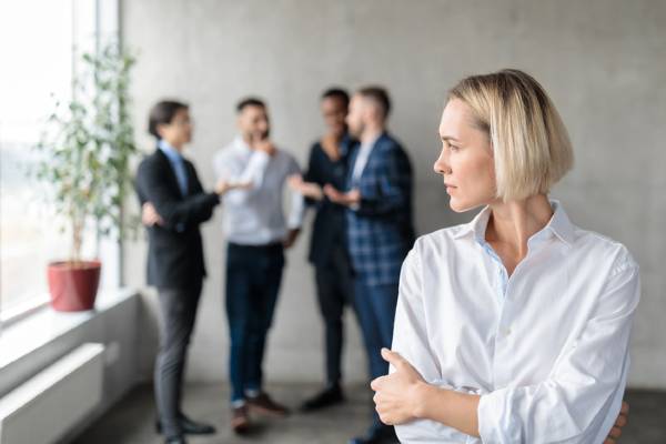Male coworkers whispering behind back of female coworker.