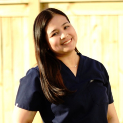 A woman in blue scrubs near a fence.
