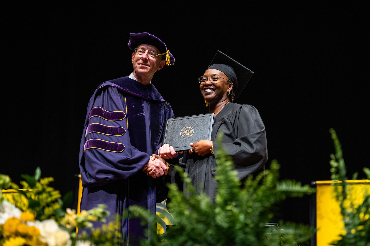 A Purdue Global graduate smiles onstage.