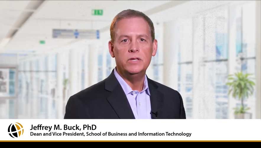 video still of Dean Jeffrey Buck in a long window-lined hallway