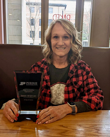 Sherry sits at a restaurant table, posing with a clear glass plaque that honors her 19 years of service at her job.