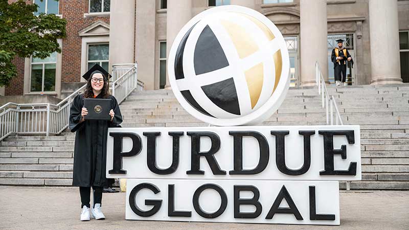 At Purdue Global’s Spring 2025 Commencement ceremony, Lauryn DeLuca shows off her diploma next to the Purdue Global sign. (Purdue Global photo/Kelsey Lefever)