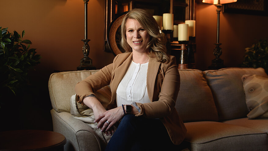 Holly Hall in a tan blazer sitting on a leather couch