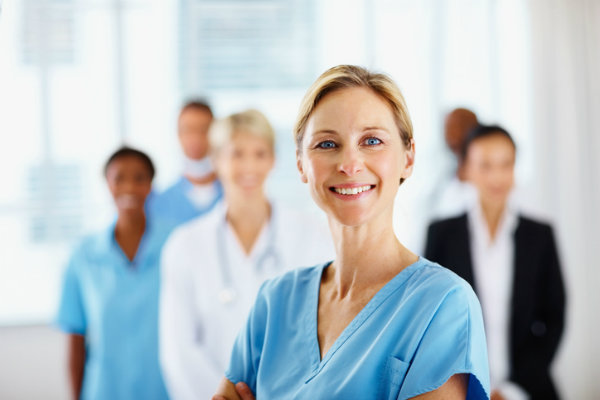 A middle-aged female nurse smiling with colleagues in the background.