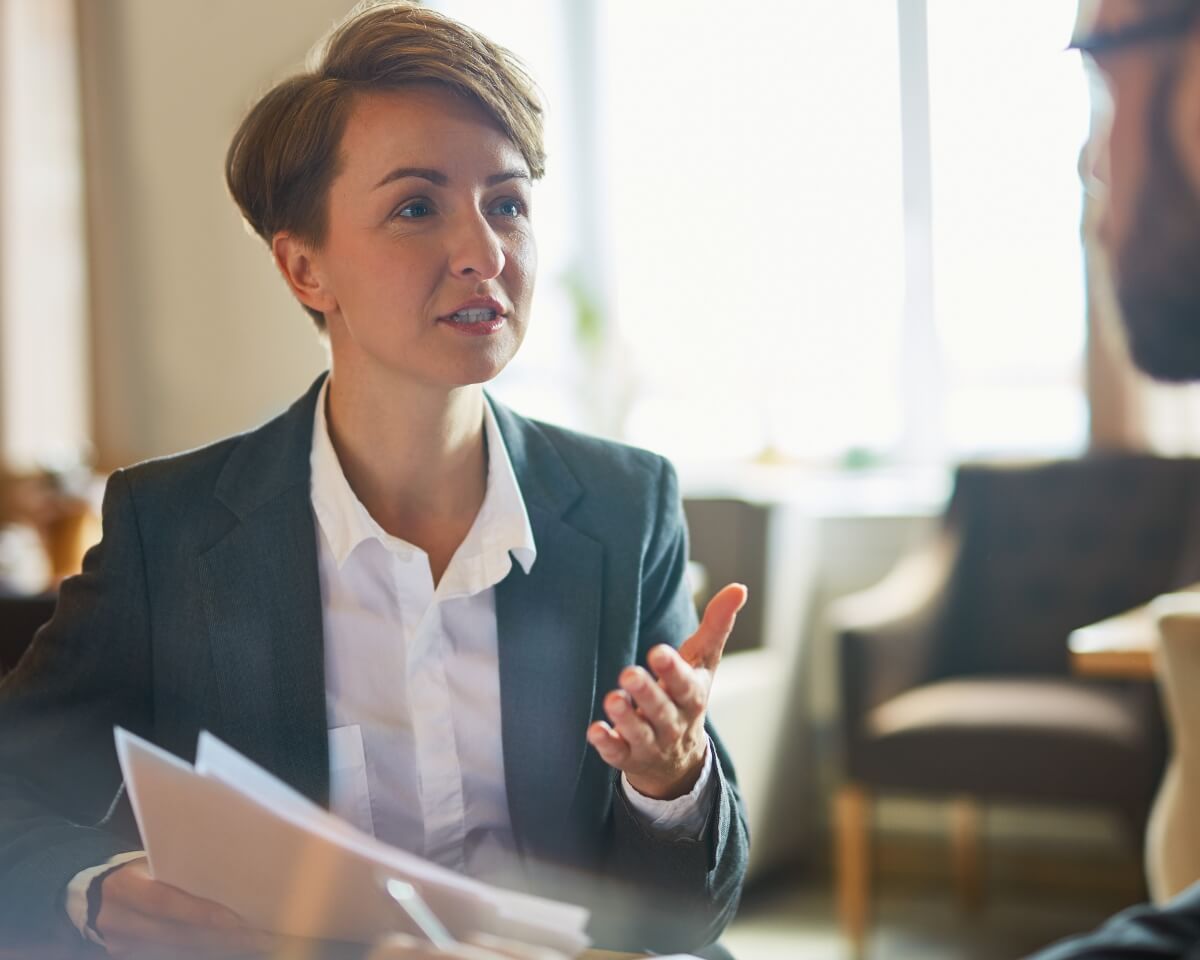 A finance professional holding documents explains something to a colleague