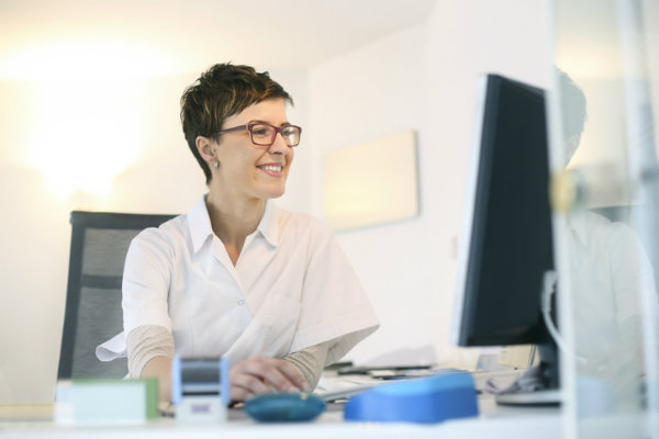 A woman sits at a desk and looks at a computer