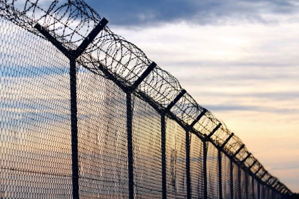A prison's barbed wire fence and a cloudy sky.