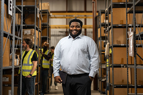 image of business professional in a warehouse full of boxes, with workers in a safety vests in the background