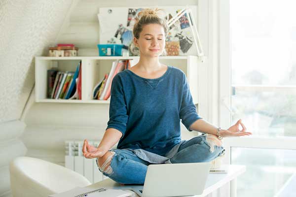 A woman sits cross-legged on a desk while meditating.