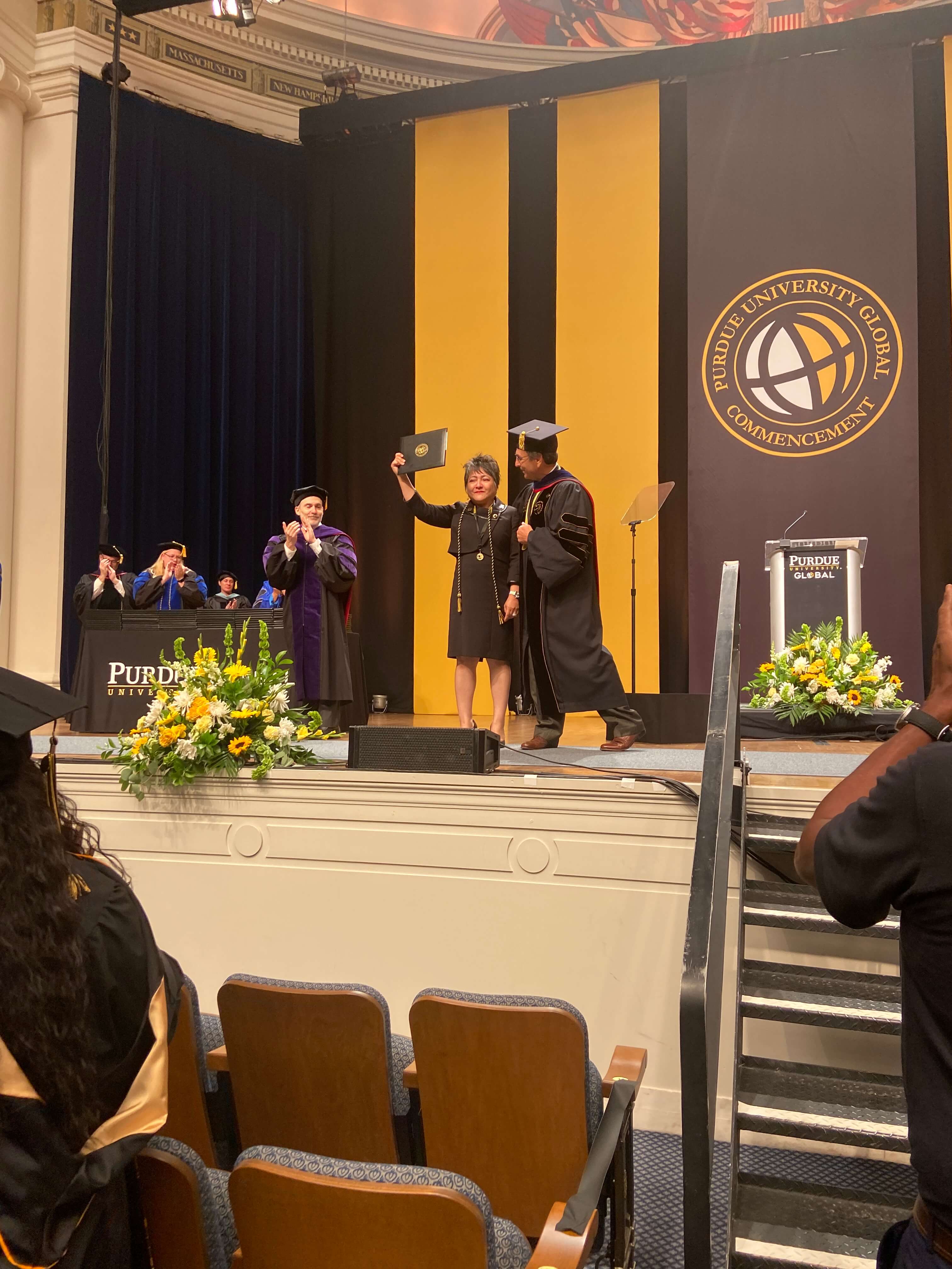 A woman holds a diploma at a Purdue Global graduation.
