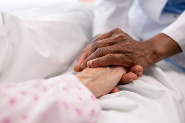Close-up of a hospice nurse holding the hand of a sick woman in bed at the hospital.