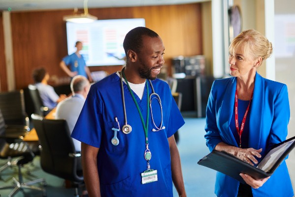 A hospital administrator stands next to a nurse wearing scrubs.