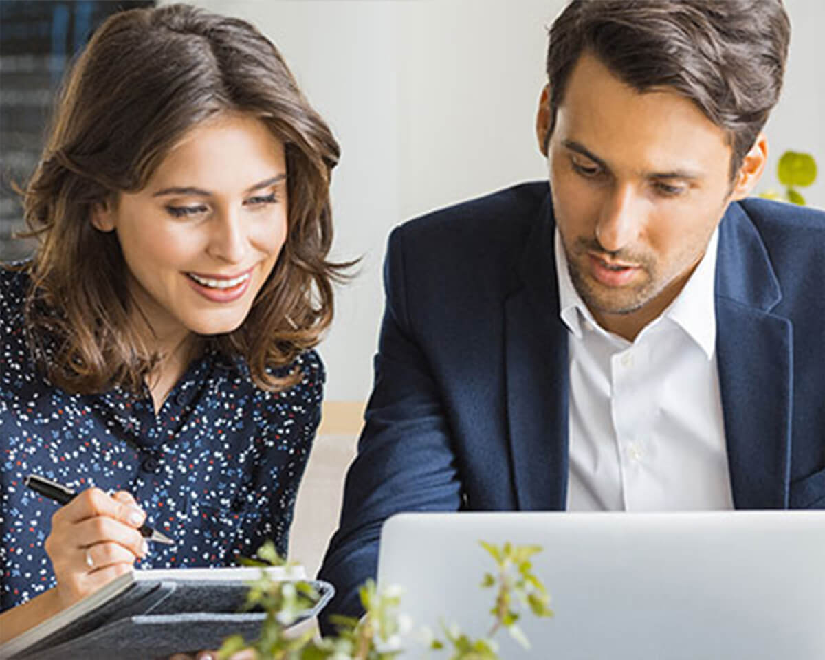 Two business professionals reviewing documents on a laptop and taking notes