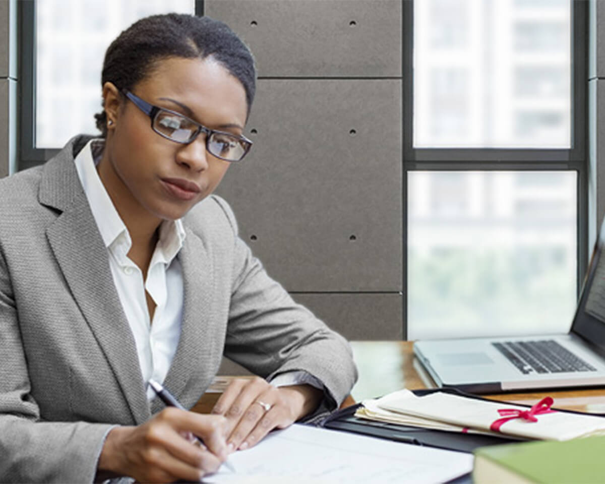 legal professional in a suit taking notes in an office with an open laptop nearby