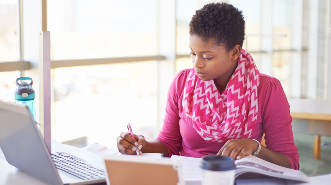 A woman working on her research paper using various sources.
