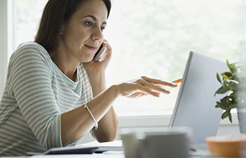 Women on the phone pointing at her laptop with a pencil