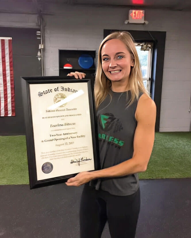 Newhart is holding a framed certificate while standing in the gym. 
