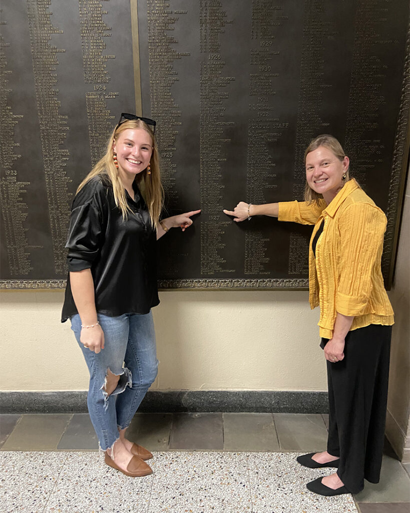 Holly Vosburgh (left) and Erin Edwards point to Maurice Woodward’s name on a plaque at the Purdue Memorial Union. (Photo provided)