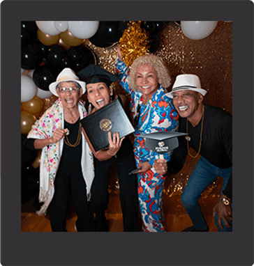 four smiling Purdue Global graduates at the Black and Gold celebration, surrounded by black and gold ballooons