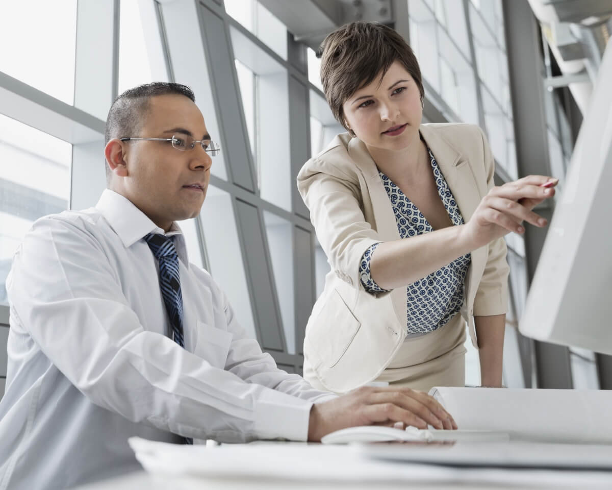 Two professionals discuss something on a computer monitor in an office