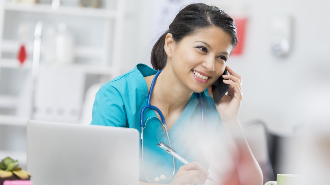 A nurse talking on the phone while working on a laptop.
