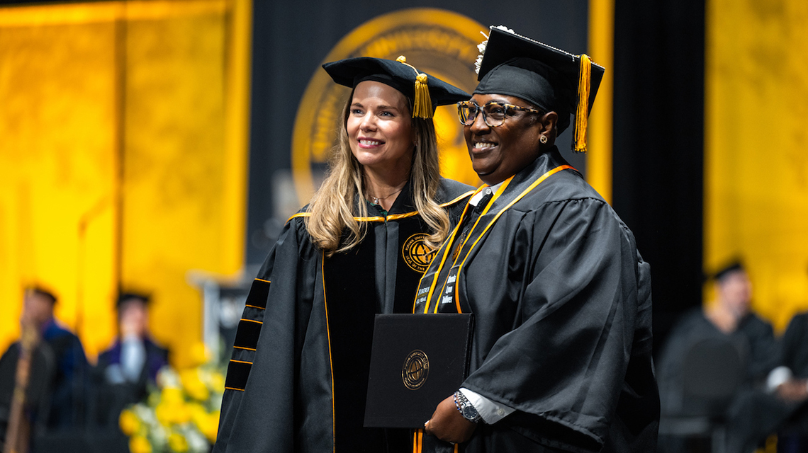 Two people in black robes standing at Purdue Global commencement.