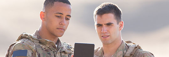 two military members in camo looking at a device