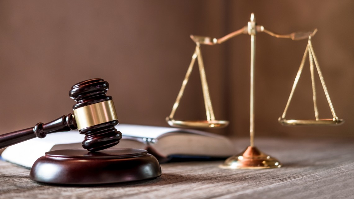 A judge's gavel next to an open law book and brass balance scales.