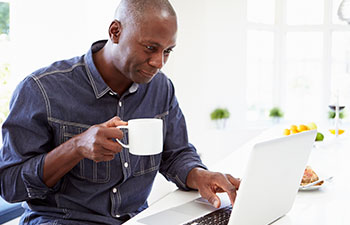 student working on a laptop at home while drinking coffee