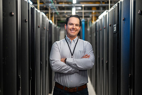 IT professional standing between rows of network equipment