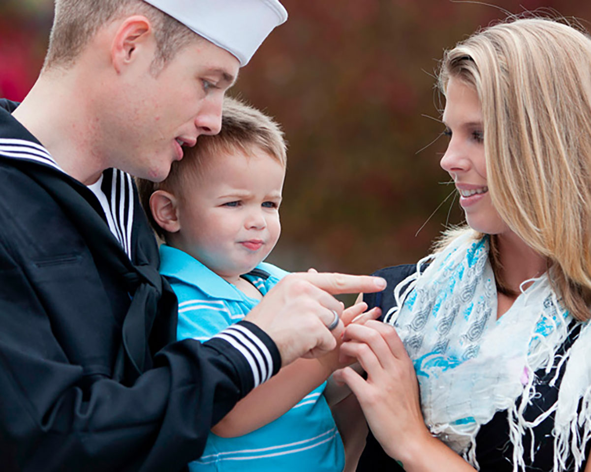 a father in a navy uniform with his wife, holding their toddler son
